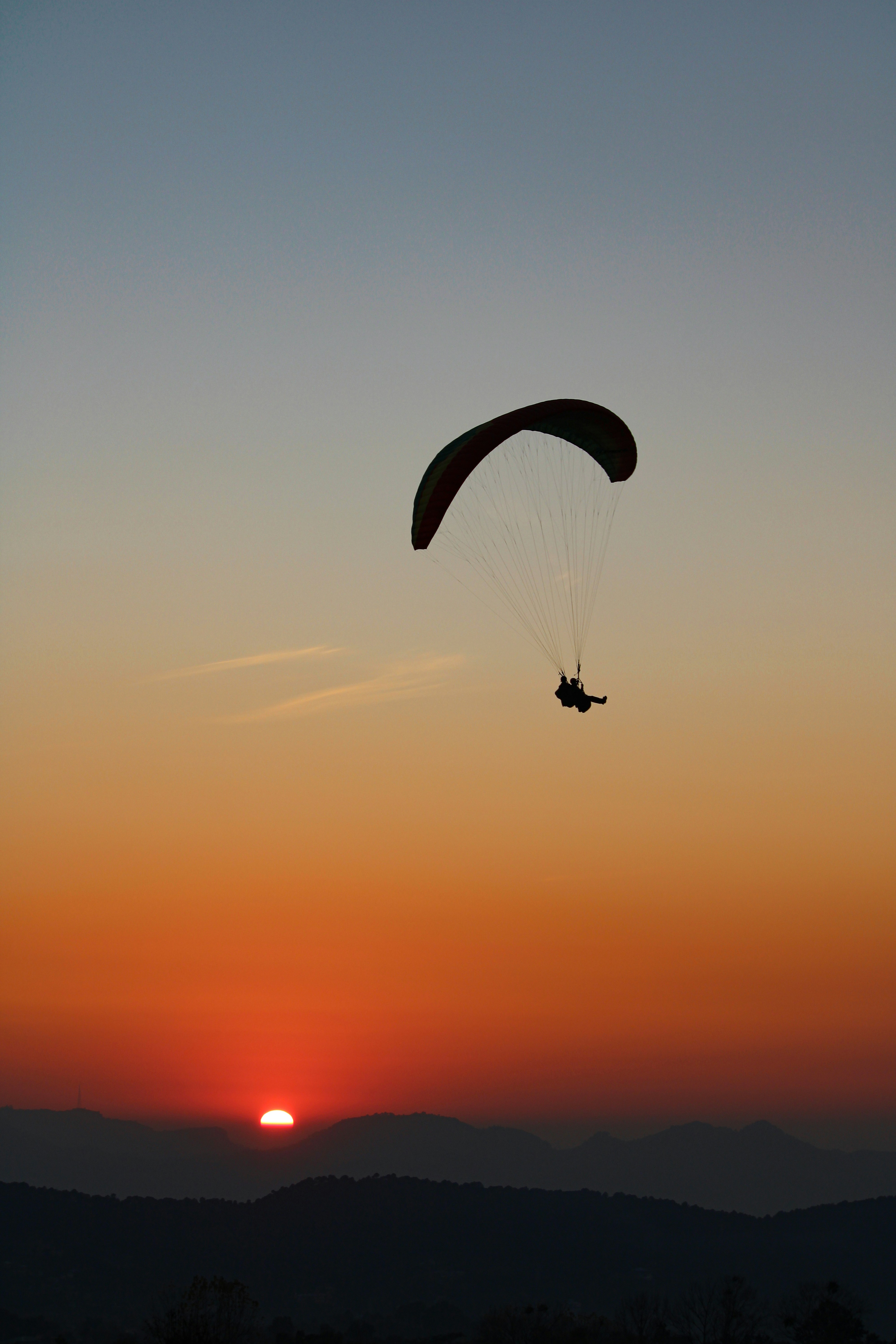 silhouette of person riding parachute during sunset