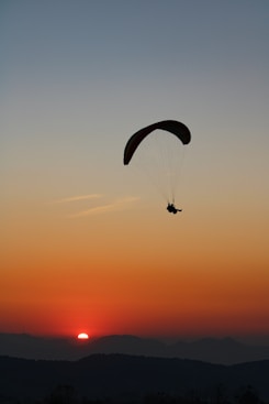 silhouette of person riding parachute during sunset