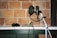 A recording studio setup featuring a microphone mounted on a stand with a pop filter, a pair of headphones, and an audio mixer resting on a white shelf. The background is a brick wall, giving the scene a rustic and professional studio vibe.
