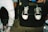 A close-up of two individuals wearing casual clothing. One person is seated on a speaker wearing white sneakers with black accents and ripped jeans. The other person stands next to them, wearing multicolored sneakers and lighter jeans. The setting appears to be casual and informal.