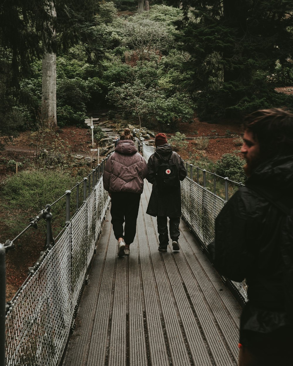 woman in black jacket walking on brown wooden bridge