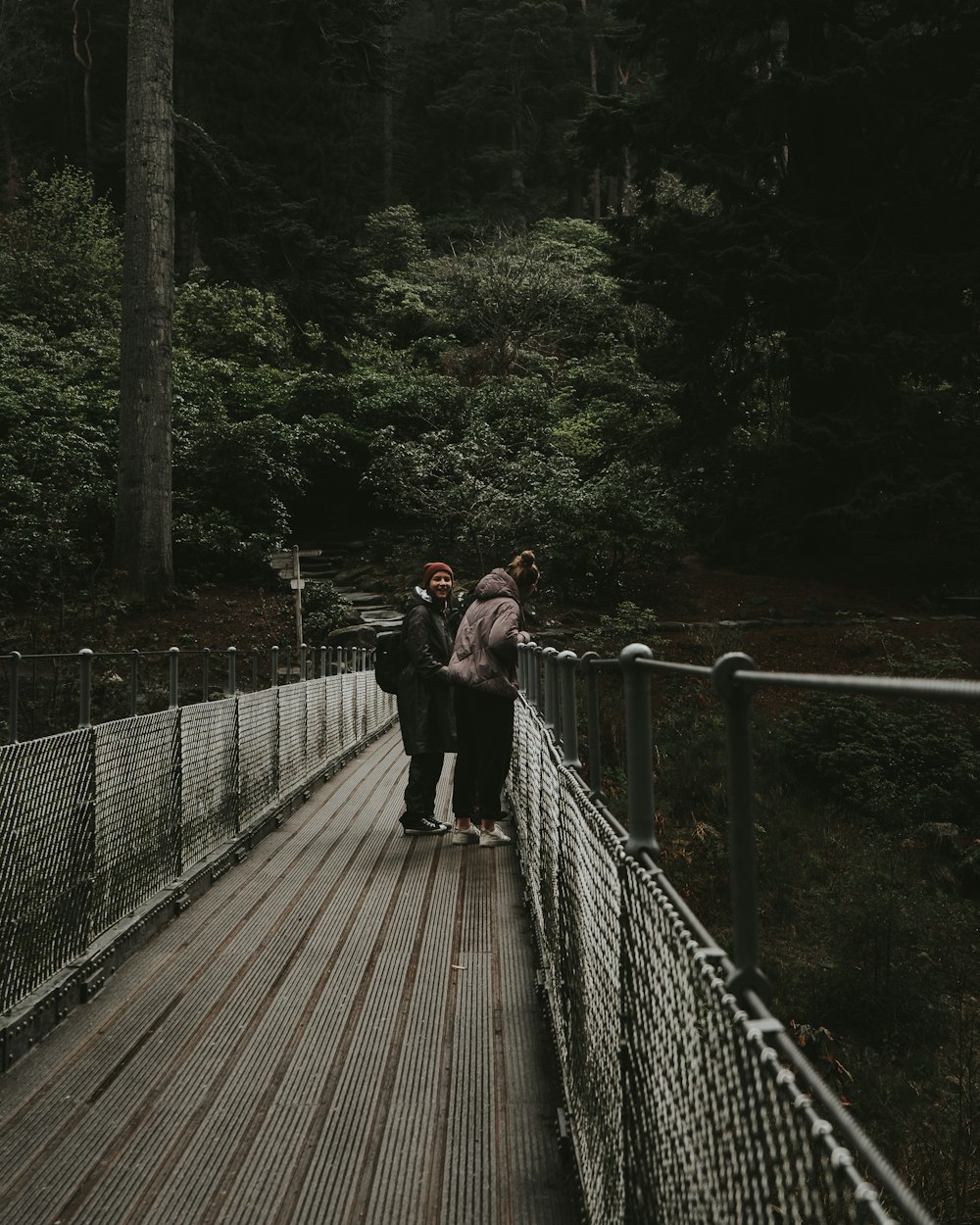 woman in black jacket and black pants walking on brown wooden bridge