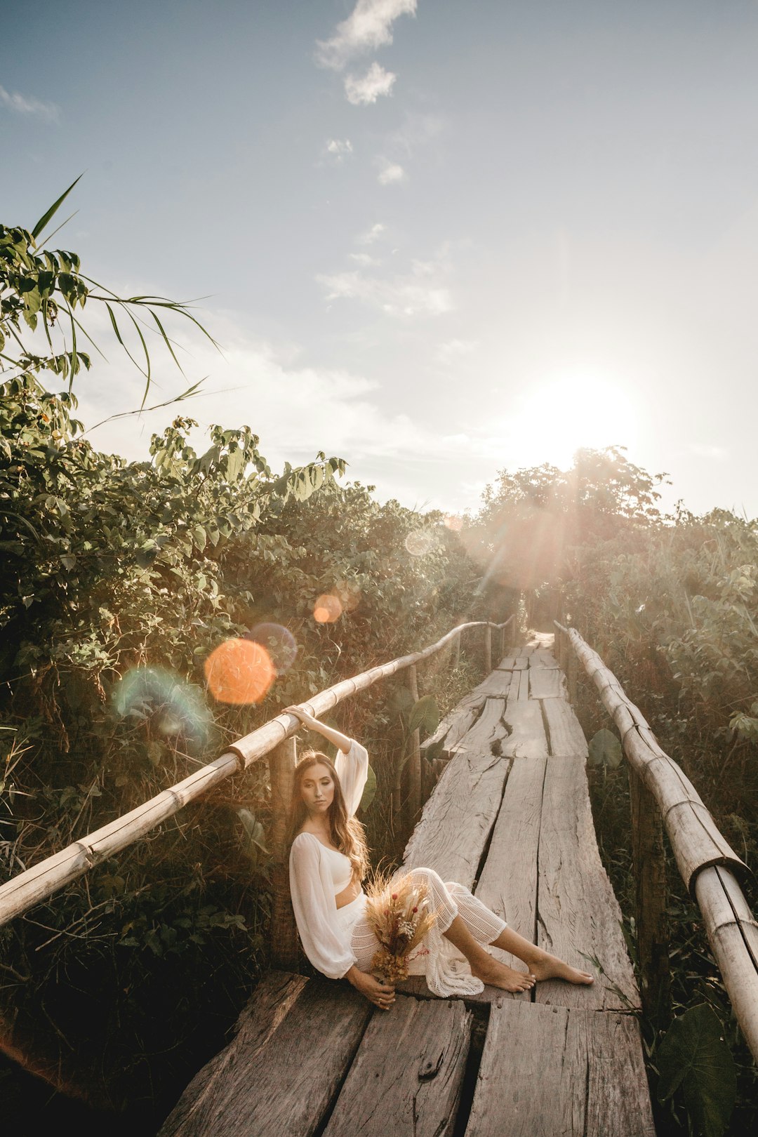 woman in white dress sitting on brown wooden fence during daytime