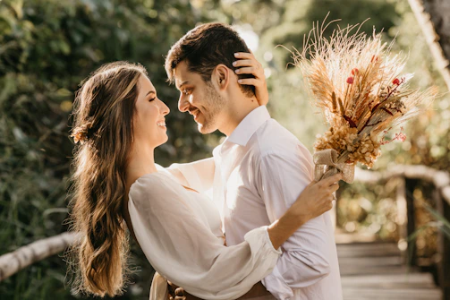 A joyful couple holding their personalized wedding invitation cards, smiling in a sunlit garden setting.