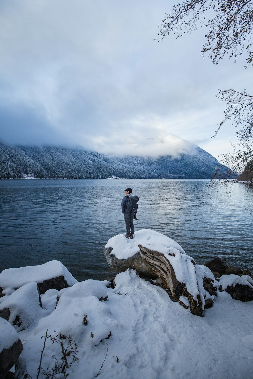 man in black jacket standing on gray rock near body of water during daytime