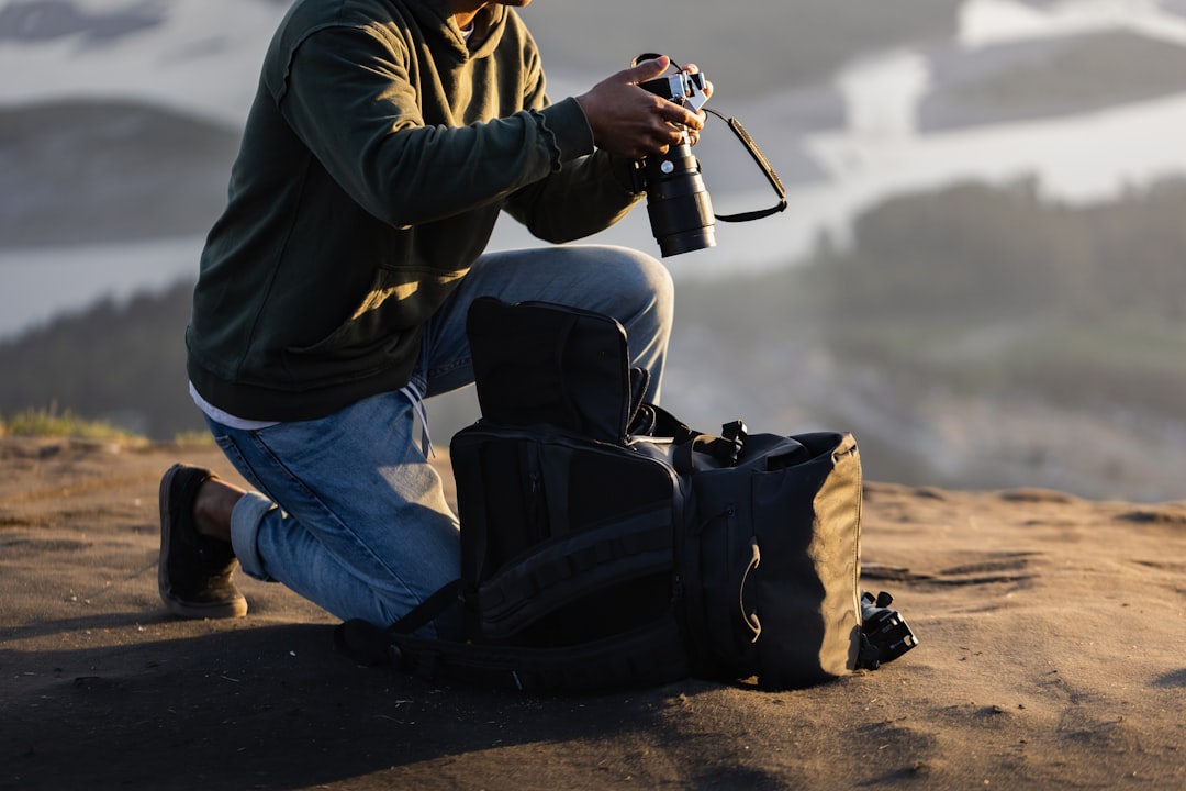 man in black jacket and blue denim jeans holding black dslr camera