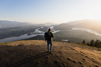 A candid photo of a traveler standing on a mountain ridge overlooking a lush Latin American valley at sunset.