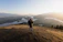 Smiling woman with a backpack overlooking a scenic mountain valley at sunrise.
