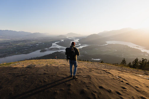 A candid photo of a traveler standing on a mountain ridge overlooking a lush Latin American valley at sunset.