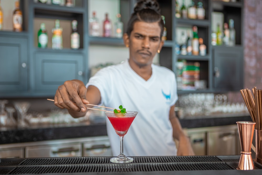 homme en t-shirt à col rond blanc tenant un bol en verre transparent avec un liquide rouge