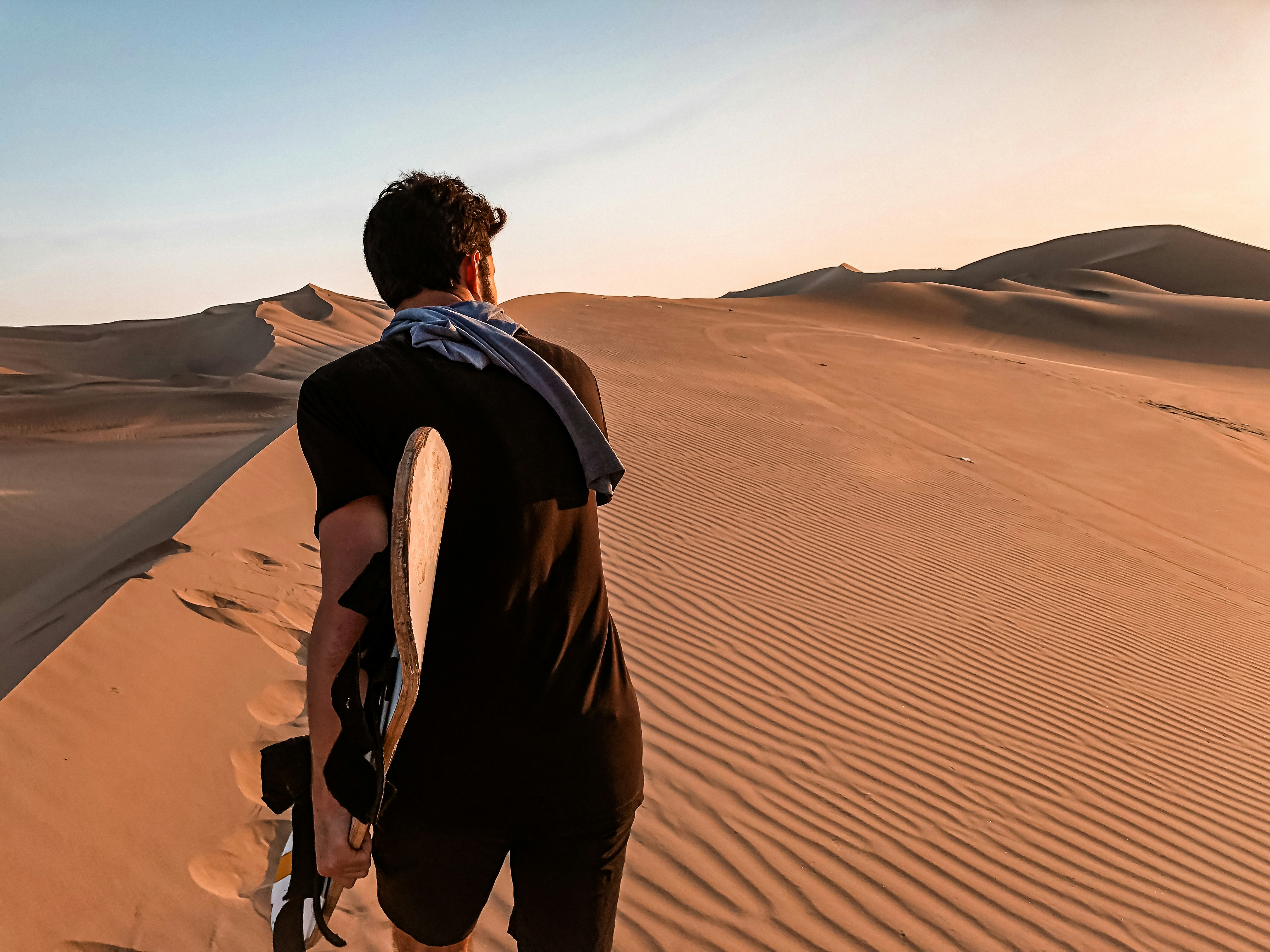 man in black jacket walking on desert during daytime, Sand boarding in Peru