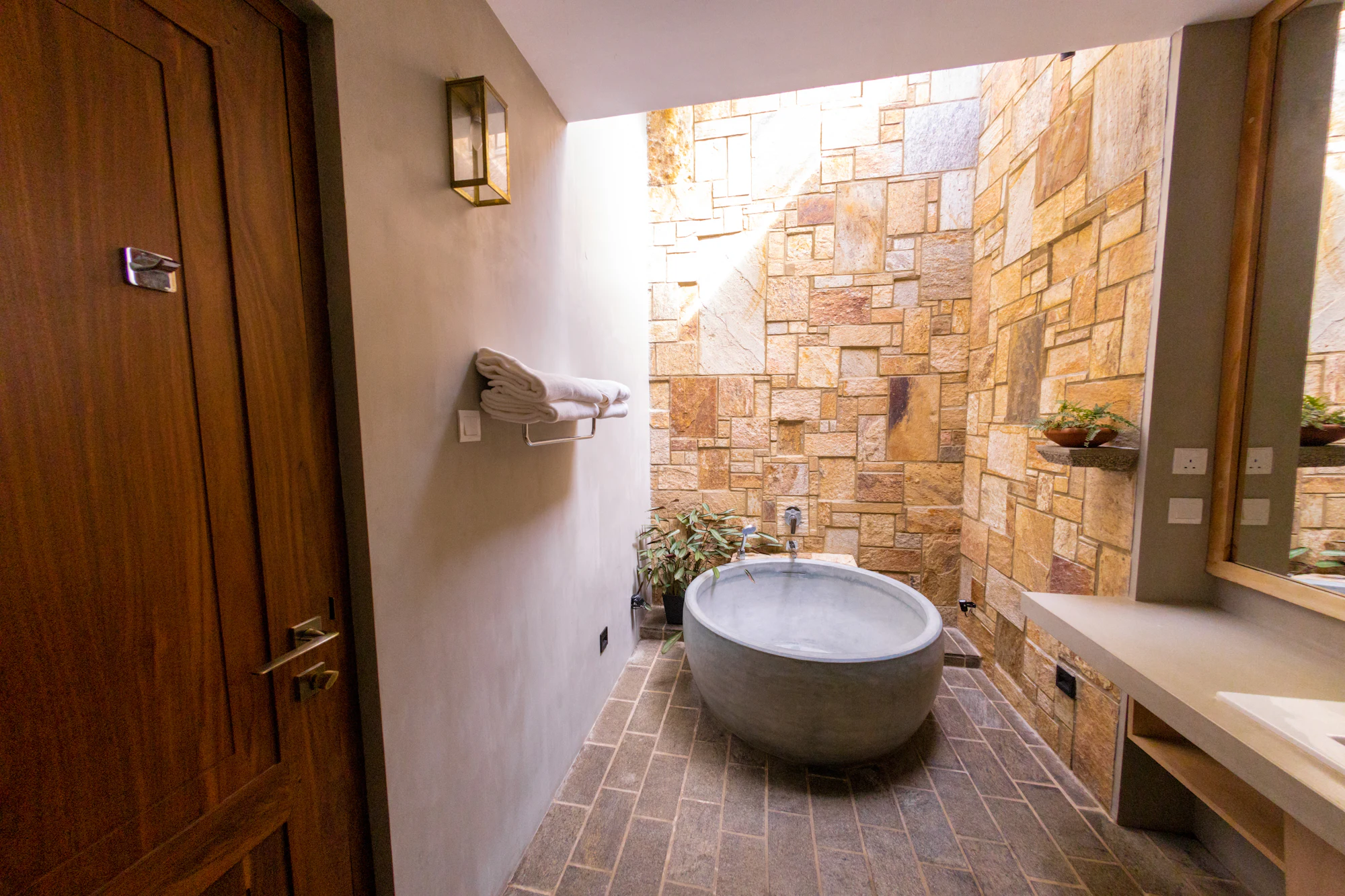 A bathroom with a deep stone tub beneath a roof light and a hand-laid stone wall