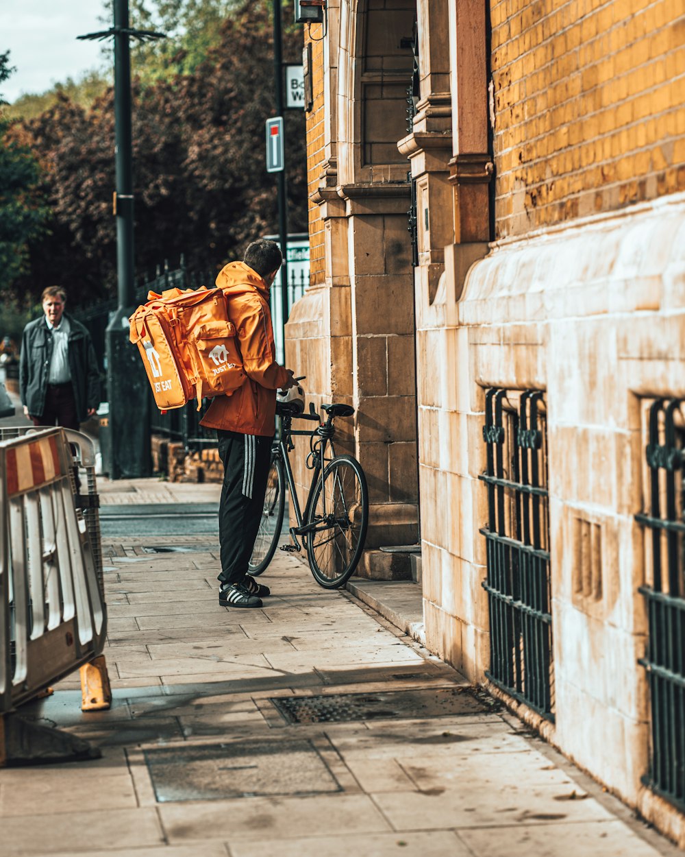 Homme en manteau orange et pantalon noir debout à côté d’un vélo noir pendant la journée