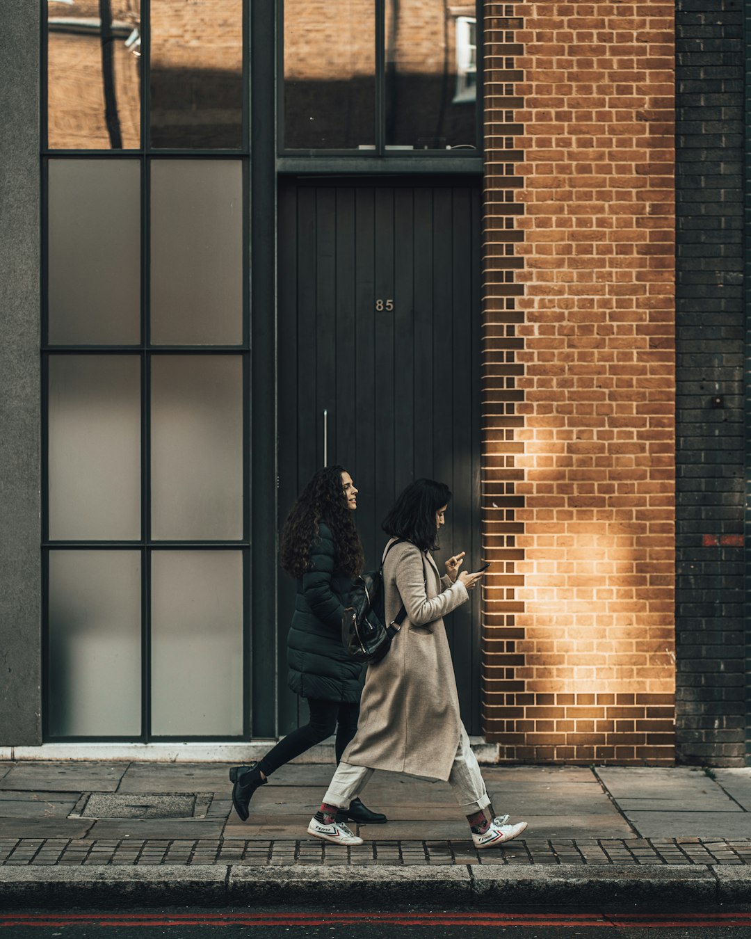 woman in gray coat and black pants sitting on brown brick wall during daytime