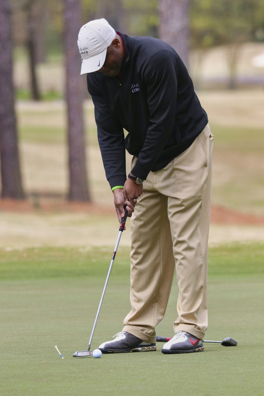 검은 재킷과 베이지색 바지를 입은 남자가 낮에 골프를 친다
