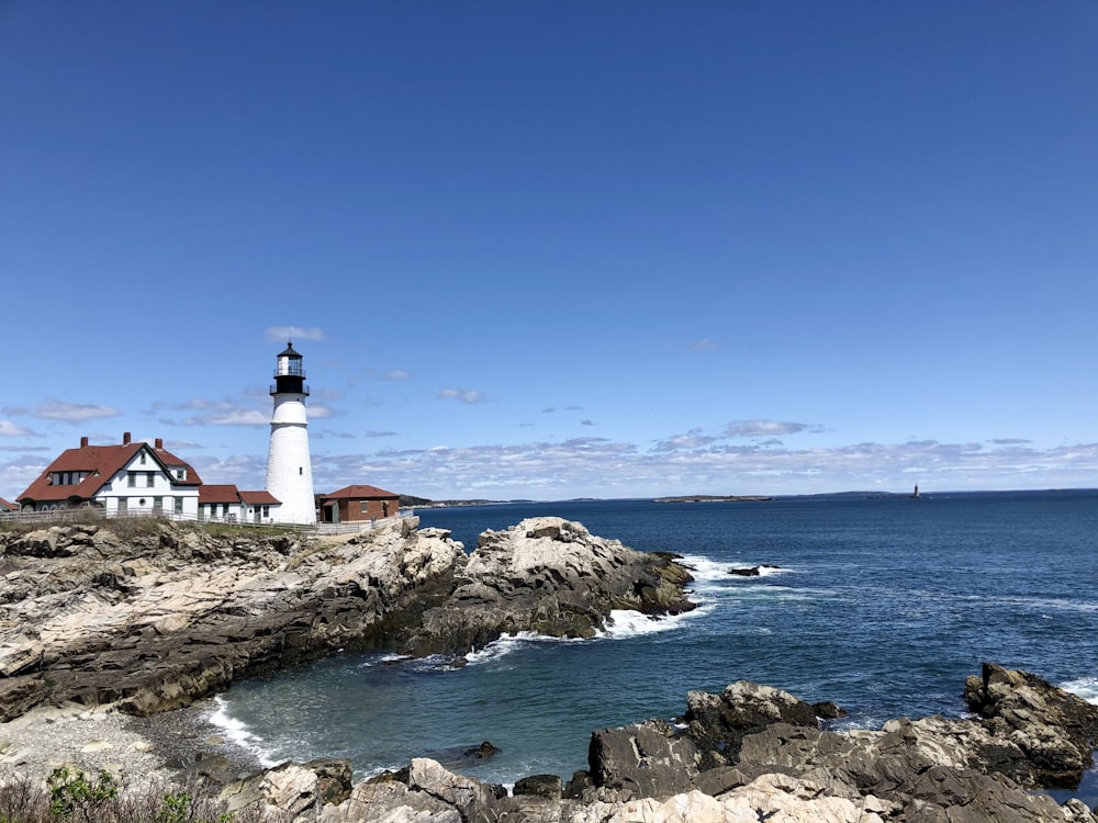 white and black lighthouse on rocky shore under blue sky during daytime