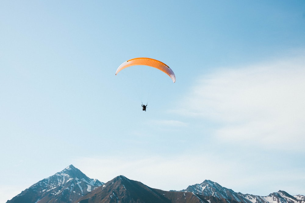 person riding orange parachute over the mountains during daytime