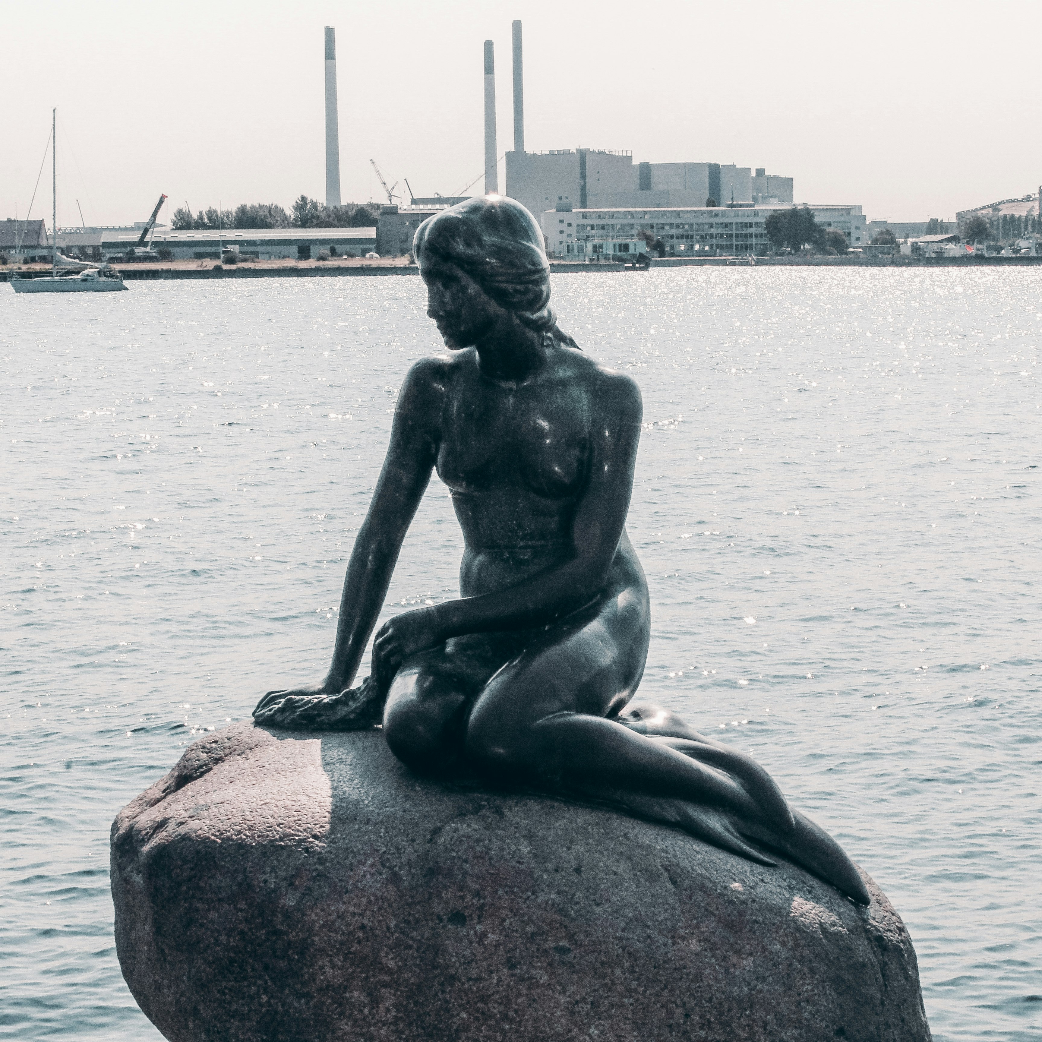 statue of woman sitting on rock near body of water during daytime