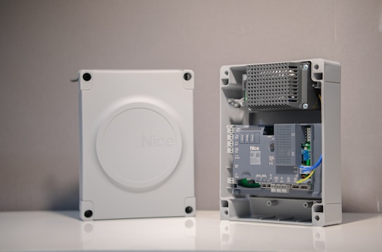 An electronic enclosure with a protective cover removed to reveal internal components. The cover is light gray and features the word 'Nice.' Inside, there are circuit boards, wires, and other electronic components organized neatly.
