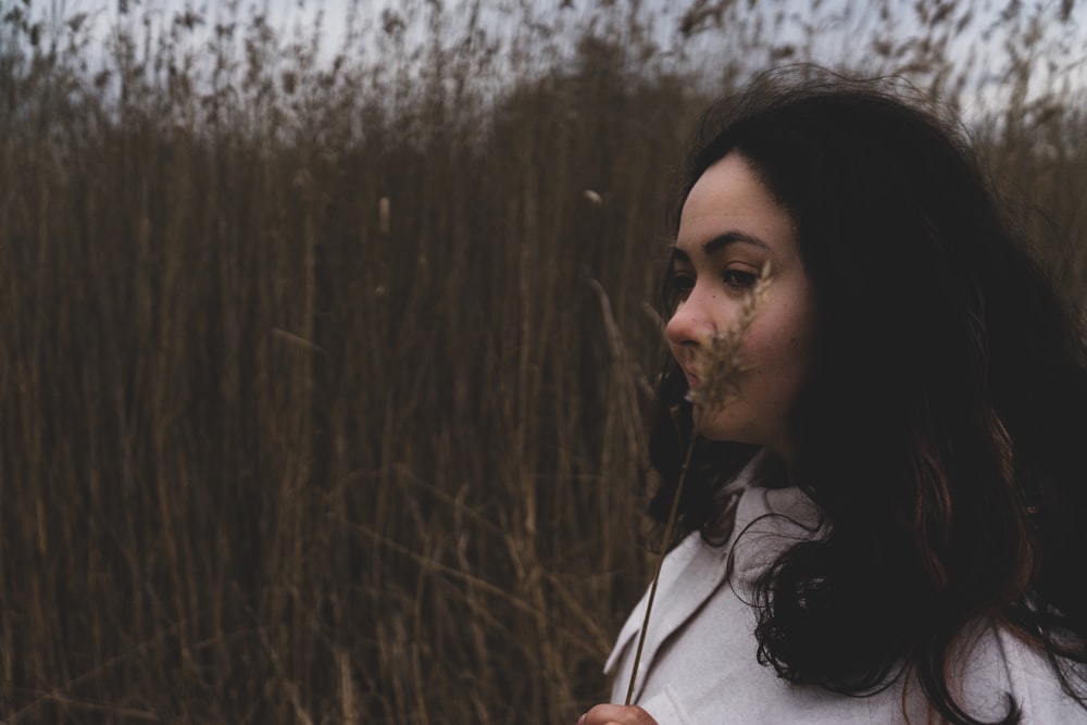 woman in white shirt standing near brown grass during daytime