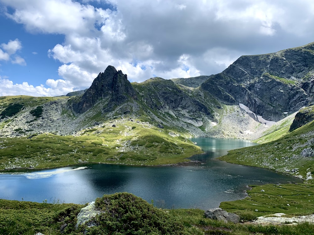 green and gray mountain near lake under white clouds and blue sky during daytime