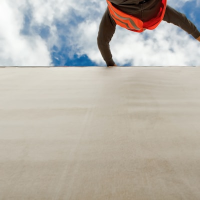 man in orange and black jacket and blue denim jeans jumping on gray concrete floor under