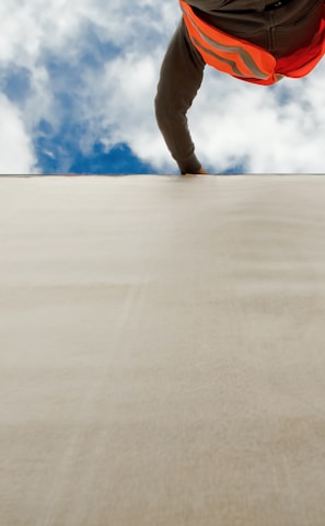 man in orange and black jacket and blue denim jeans jumping on gray concrete floor under