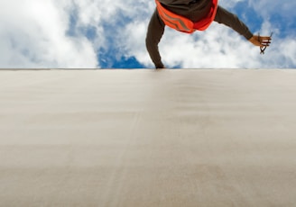 man in orange and black jacket and blue denim jeans jumping on gray concrete floor under