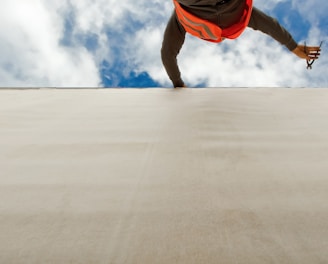 man in orange and black jacket and blue denim jeans jumping on gray concrete floor under