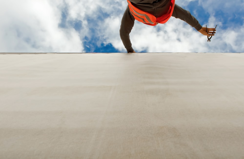 man in orange and black jacket and blue denim jeans jumping on gray concrete floor under