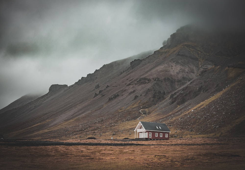 white and brown wooden house near brown mountain under white clouds during daytime