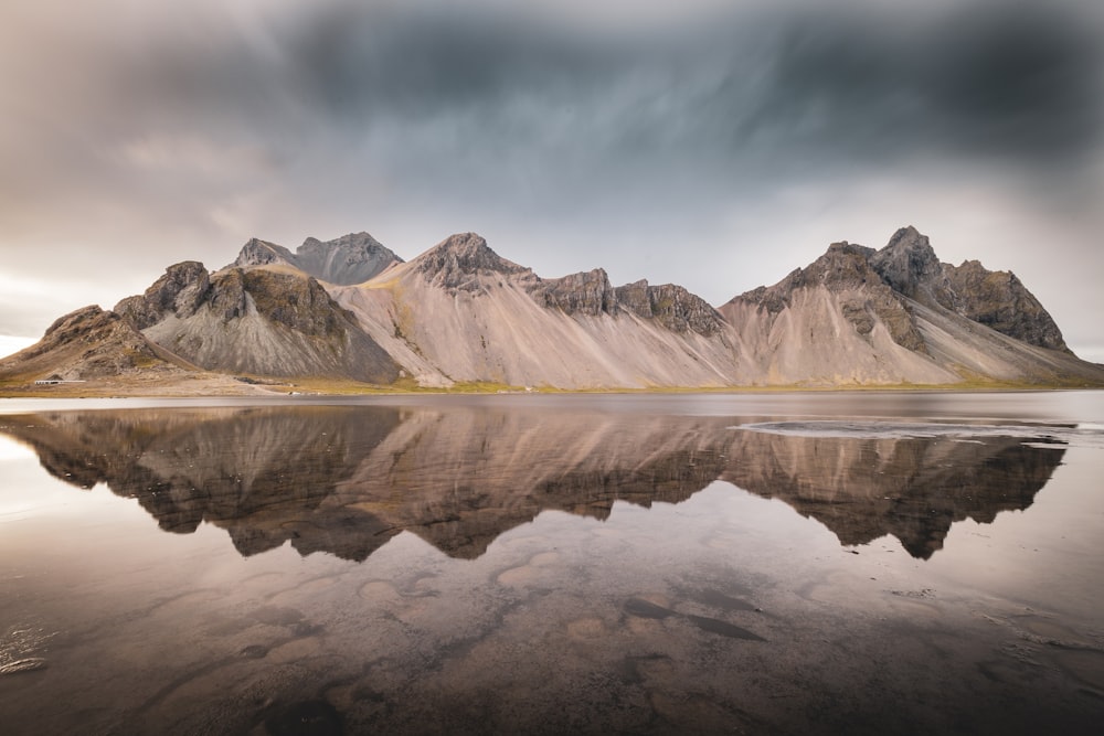 montagne marroni e bianche vicino allo specchio d'acqua sotto le nuvole bianche durante il giorno