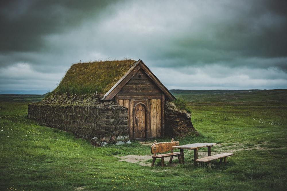 brown wooden bench on green grass field near brown wooden house under gray cloudy sky