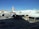 An Asiana Airlines aircraft is stationed at an airport gate. The airplane is undergoing maintenance or loading, with equipment and vehicles around it. Several ground support trucks and cargo loaders are positioned beside the aircraft. The sky is clear, and nearby are buildings and other parked aircraft.