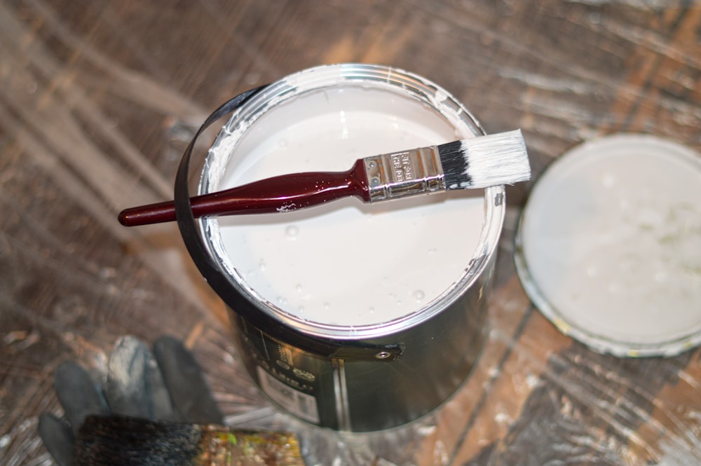 red handle paint brush in white paint bucket