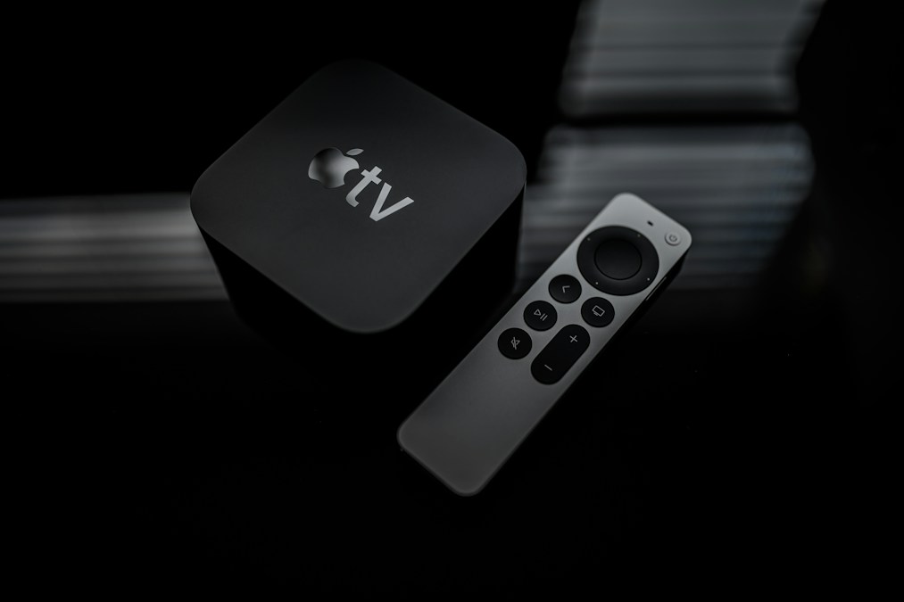 Un boîtier Apple TV noir et sa télécommande Siri Remote posés sur une surface sombre (photo d'illustration d'un modèle précédent)