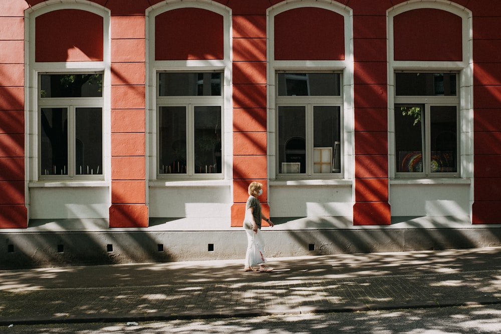 昼間、赤と白のコンクリートの建物の近くの歩道を歩く赤いドレスを着た女性