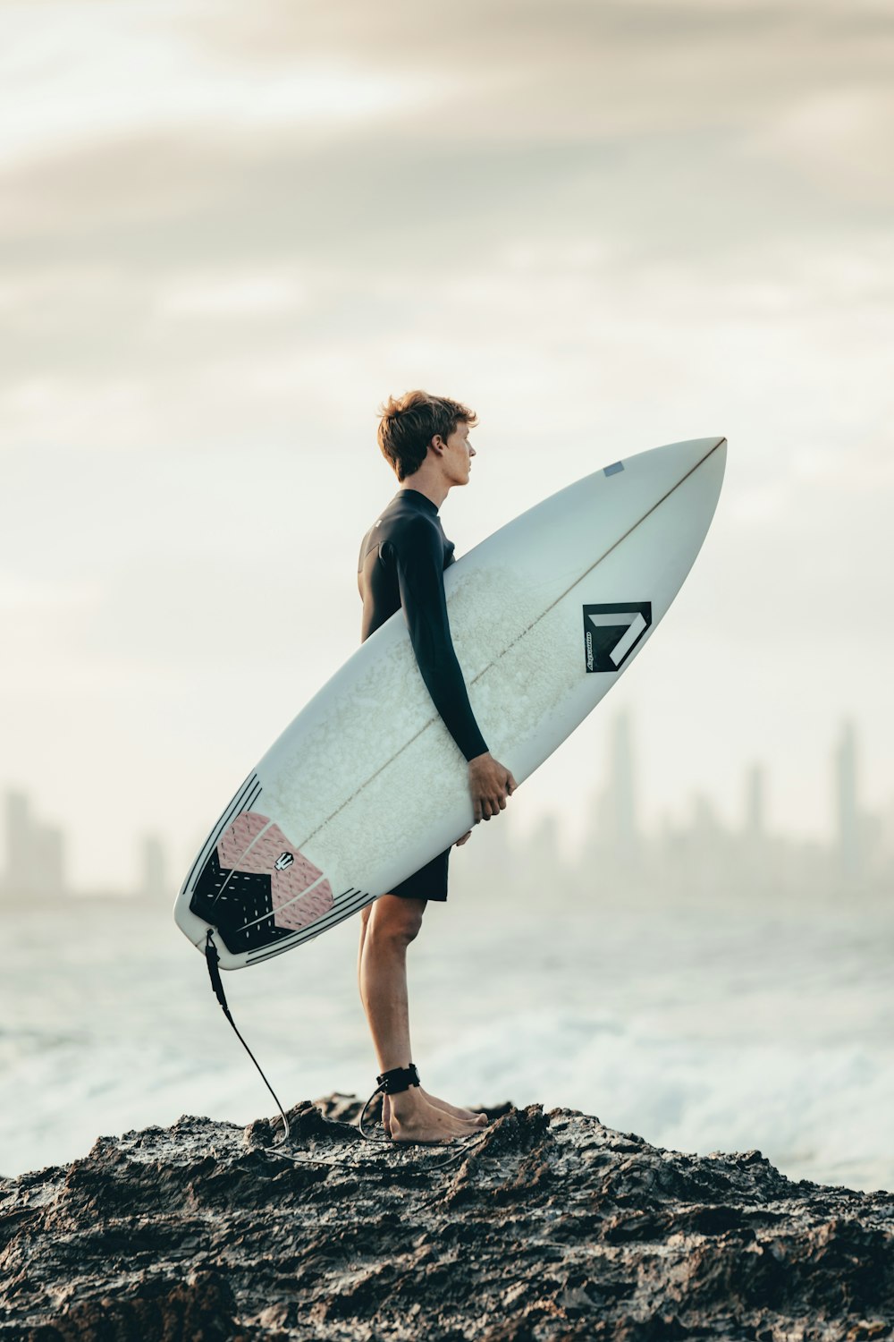 femme en débardeur noir portant une planche de surf blanche