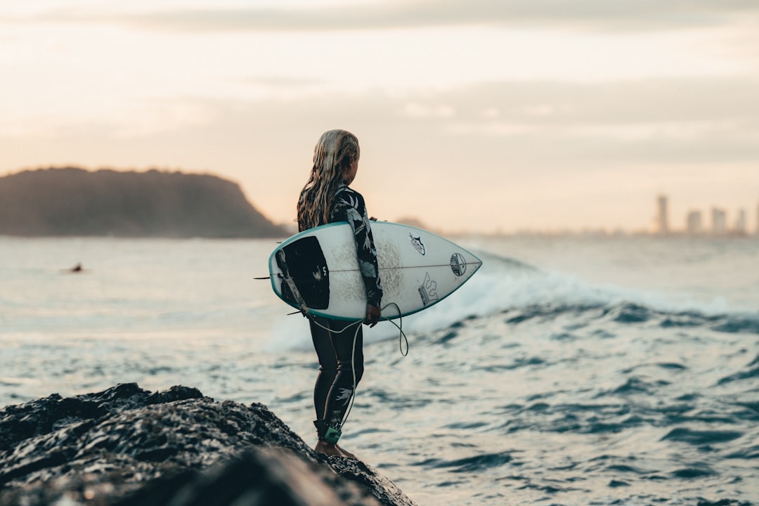 woman in black wet suit carrying white surfboard on seashore during daytime