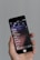 A person holds a smartphone displaying a music application interface, featuring a list of songs in a language that appears to be Chinese. The phone screen shows details such as song titles, artist information, and playback controls. The background is a neutral gray color.