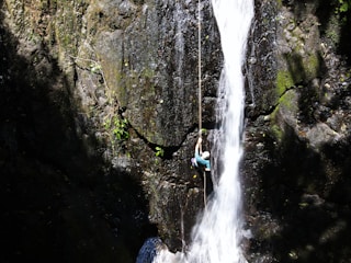 person in blue jacket and blue denim jeans standing on rock near waterfalls during daytime