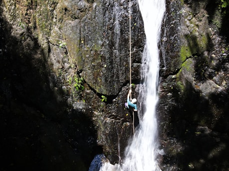 person in blue jacket and blue denim jeans standing on rock near waterfalls during daytime