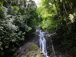 person in blue jacket standing on rock near waterfalls during daytime