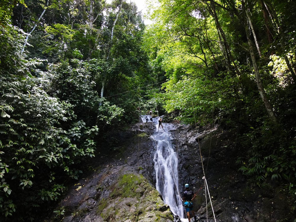 person in blue jacket standing on rock near waterfalls during daytime