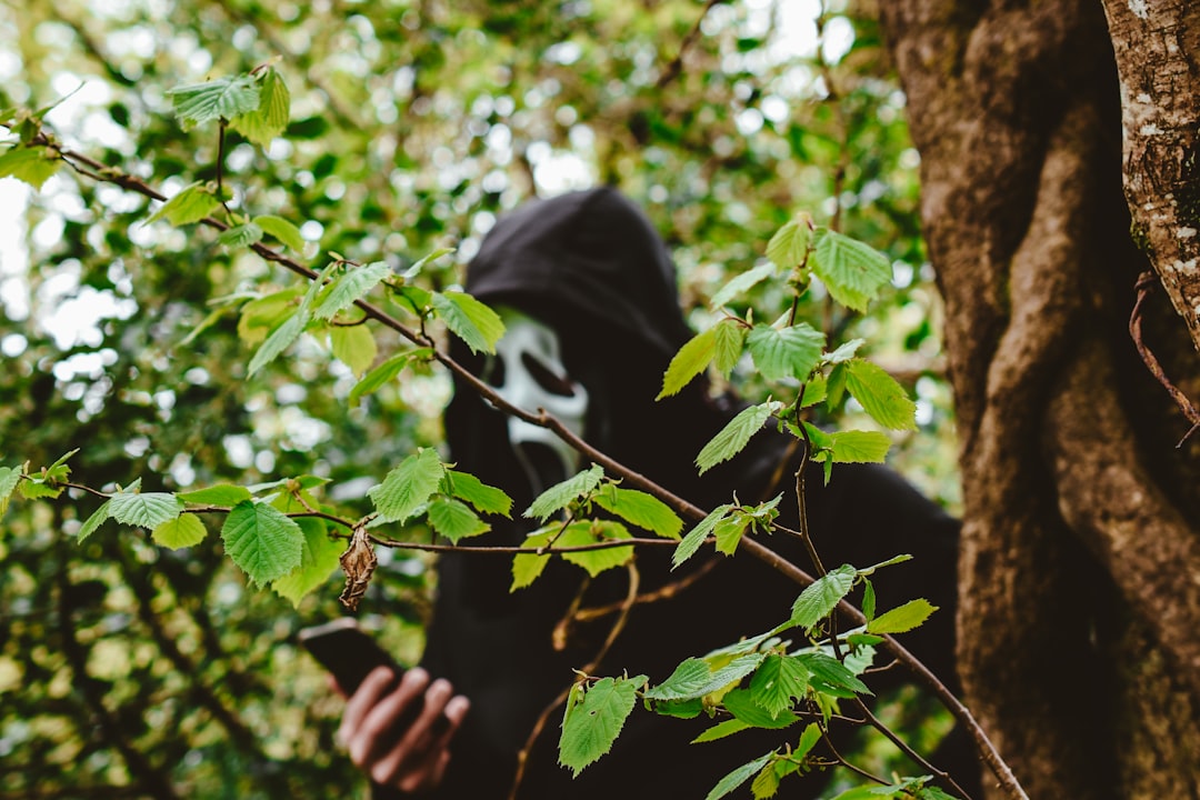 person in black hoodie hiding on green leaves during daytime