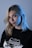 A person with blonde hair and a subtle expression is wearing a black t-shirt with a graphic design featuring the word California. The lighting casts a blue hue on their face and hair, giving a dramatic effect against a plain background.