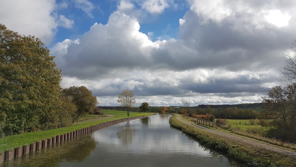 campo de hierba verde cerca del río bajo nubes blancas y cielo azul durante el día