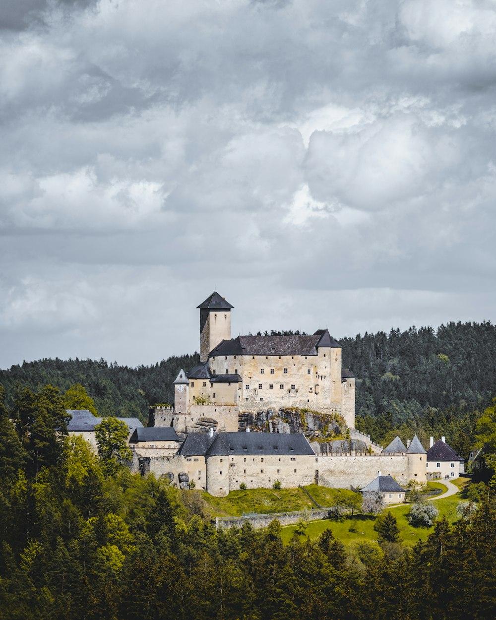 Weißes Betongebäude tagsüber umgeben von grünen Bäumen unter weißen Wolken