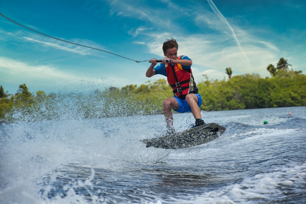 boy in red and blue shirt and blue shorts playing on water during daytime