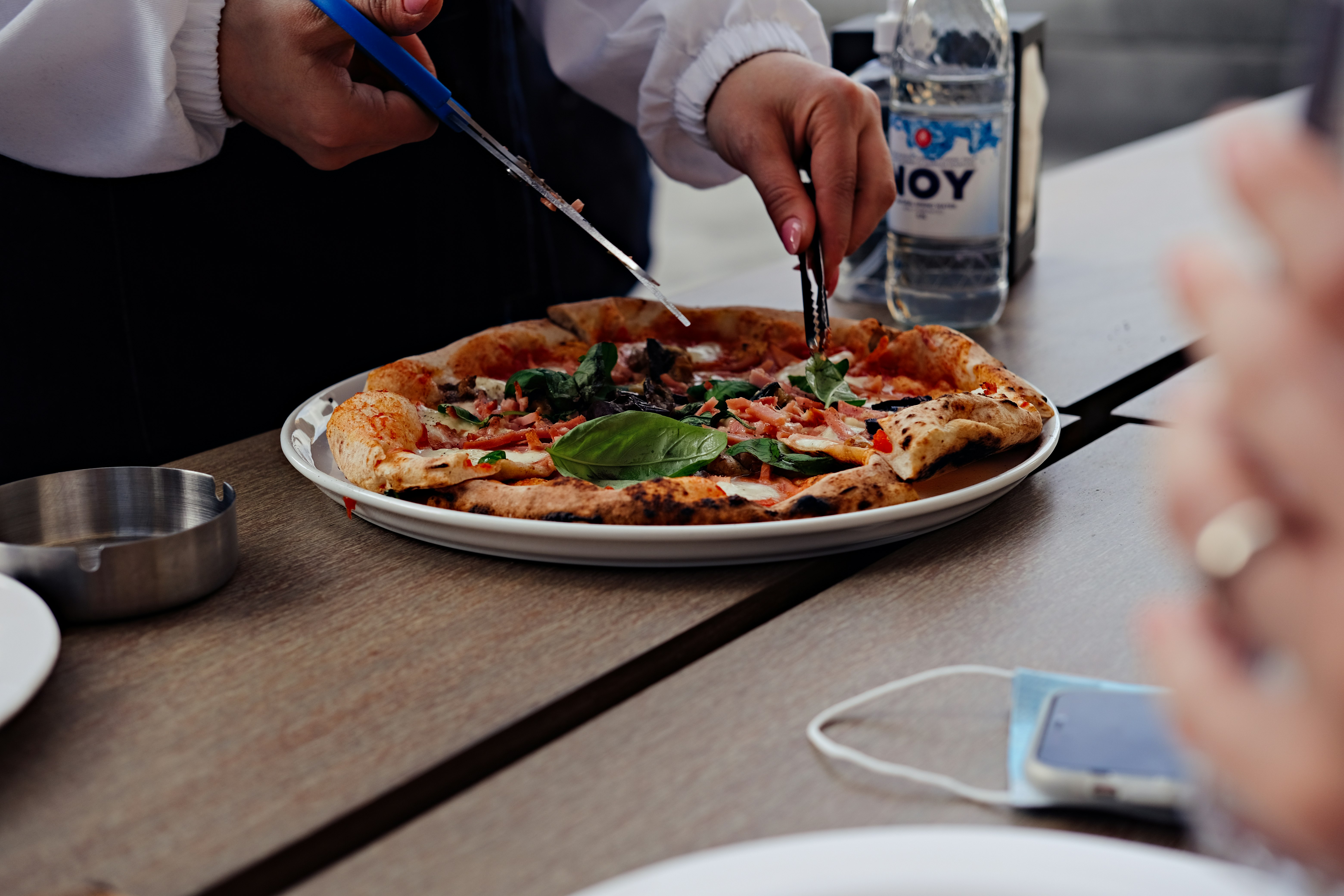 person holding blue and black chopsticks slicing pizza on white ceramic plate